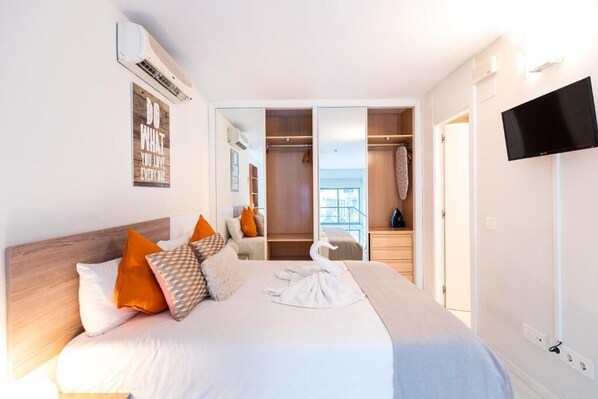 A bedroom with a large bed, a wardrobe, a television, and a view of the outdoors.