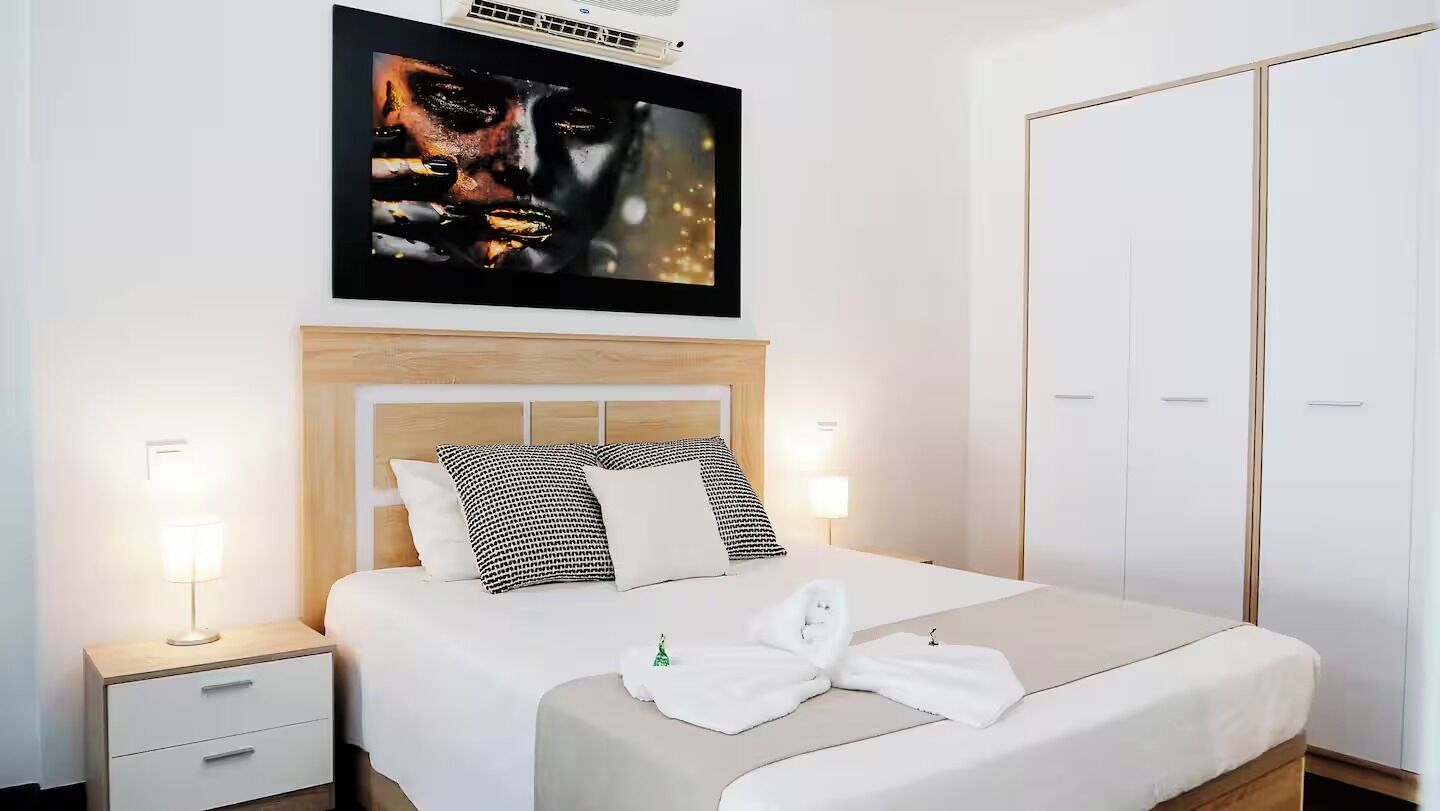 Ein Hotelzimmer mit Bett, Nachttischlampen, einem Kleiderschrank und einem an der Wand befestigten Fernseher.