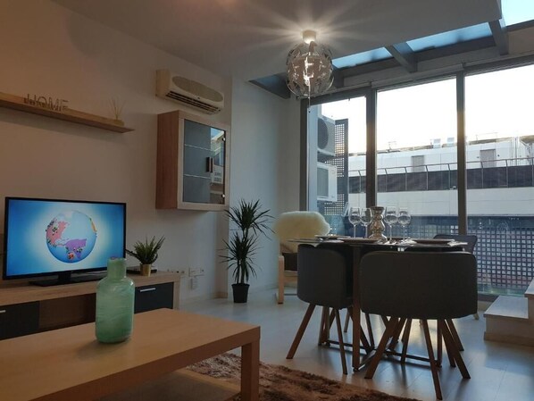 A modern living room with a flat-screen TV, a wooden coffee table, and a dining area with a glass table and chairs. - Seasonal Living Oshun Madrid Norte (Madrid)