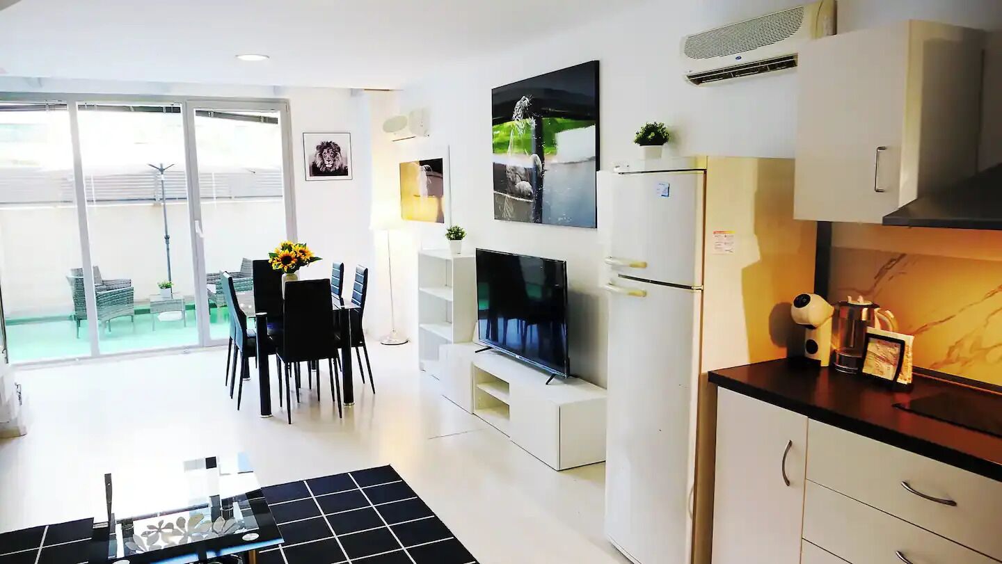 Una cocina moderna con armarios blancos, horno empotrado y comedor con mesa y sillas.