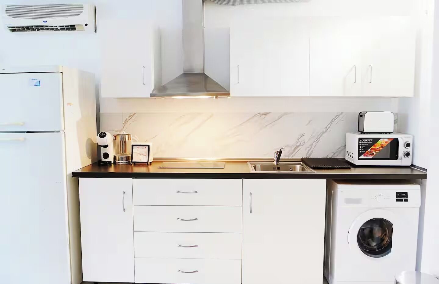 A compact kitchen with a built-in washing machine, a microwave, and a sink.