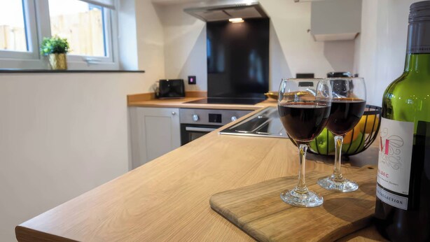 A modern kitchen with a wooden countertop, two wine glasses filled with red wine, and a bottle of wine on the right. - Ash Cottages (Llanrwst)