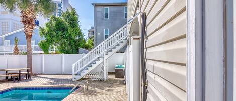 A swimming pool with a wooden deck, a white fence, and a staircase leading to a building.