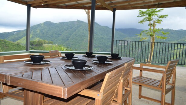 Una mesa de madera con cuencos negros y una barandilla de metal con vistas a un paisaje montañoso.