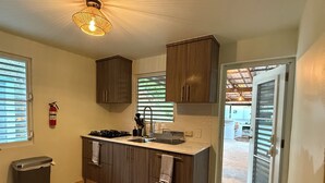 Una cocina moderna con armarios de madera, una estufa a gas y un fregadero. Hay un extintor en la pared y un cubo de basura en la esquina.