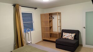 Un dormitorio con cama, armario, una silla y ventana con persianas.
