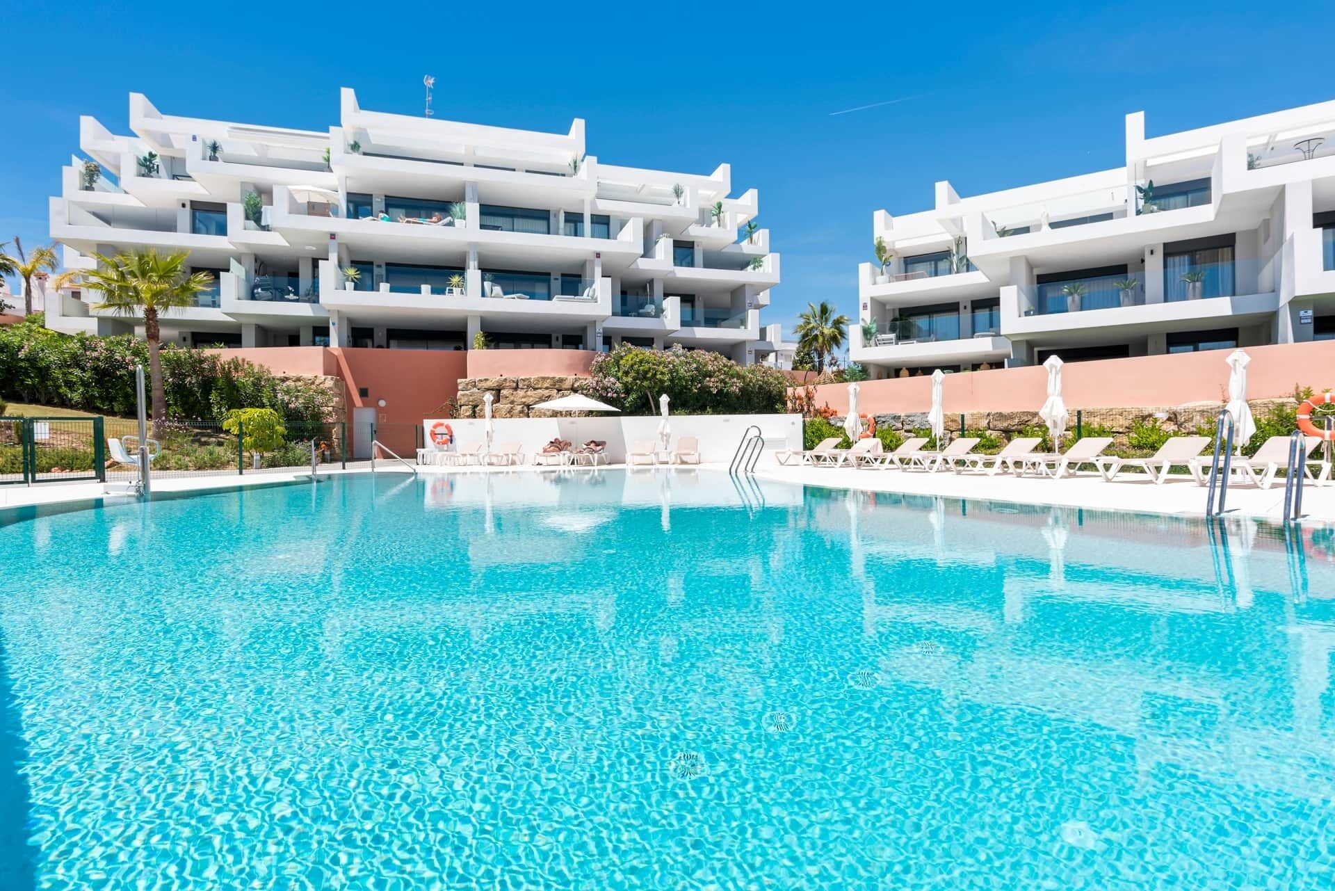 Ein modernes Hotel mit großem Schwimmbad, mehreren Balkonen und blauem Himmel.
