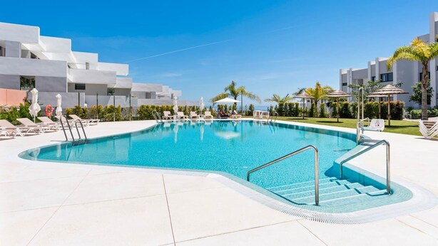 Piscina com espreguiçadeiras e guarda-sóis, cercada por edifícios modernos e palmeiras.