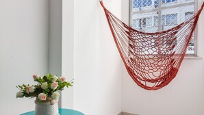 Een hoekkamer met een hangmat, een klein tafeltje met een vaas, een inlijsting foto en een raam met uitzicht op gebouwen.