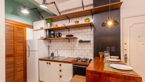 Eine kleine Küche mit weißen Schränken, einer Holz Arbeitsplatte und einem Essbereich mit Tisch für zwei Personen.