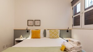 Ein ordentlich gemachtes Bett mit einer grünen Tagesdecke, zwei Kissen mit gelb-weißen Mustern und einem Stapel weißer Handtücher mit einem Ananas-Logo.
