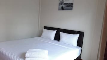 Ein ordentlich bezogenes Bett mit weißen Leinen und Kissen, ein schwarzer Kopfteil und ein gerahmtes Stadtbild an der Wand.