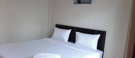 Una cama bien hecha con sábanas y almohadas blancas, un cabecero negro y un cuadro con una vista de la ciudad en la pared.