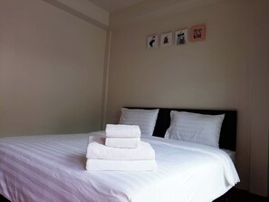 Ein ordentlich bezogenes Bett mit weißen Leinentüchern und einem Stapel gefalteter Handtücher, ein schwarzes Kopfteil und drei kleine gerahmte Bilder an der Wand.