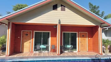 A two-story building with a swimming pool, large sliding glass doors, and a small patio area with outdoor furniture.