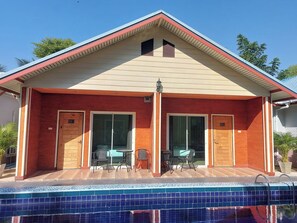 Een gebouw met twee verdiepingen, een zwembad, grote schuifdeuren en een klein terras met tuinmeubilair.