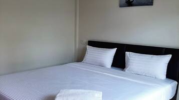 Una cama bien hecha con sábanas y almohadas blancas, una toalla doblada sobre la cama y un cuadro colgado en la pared con una vista de la ciudad.