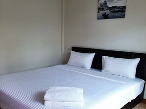 A neatly made bed with white linens and pillows, a folded towel on the bed, and a wall-mounted picture of a cityscape. - Phenwaree Amphawa Resort by Zuzu (Samut Songkhram)