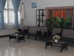 A living room with a sofa set, two coffee tables with flower vases, a large potted plant, and a wall-mounted shelf with decorative items. - Phenwaree Amphawa Resort by Zuzu (Samut Songkhram)