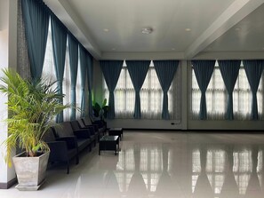 Eine geräumige Lobby mit Sitzgelegenheit, großen Fenstern mit Vorhängen und einer Zimmerpflanze.
