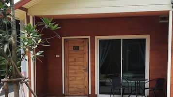 A room with a wooden door, a sliding glass door, and a small outdoor seating area with chairs.