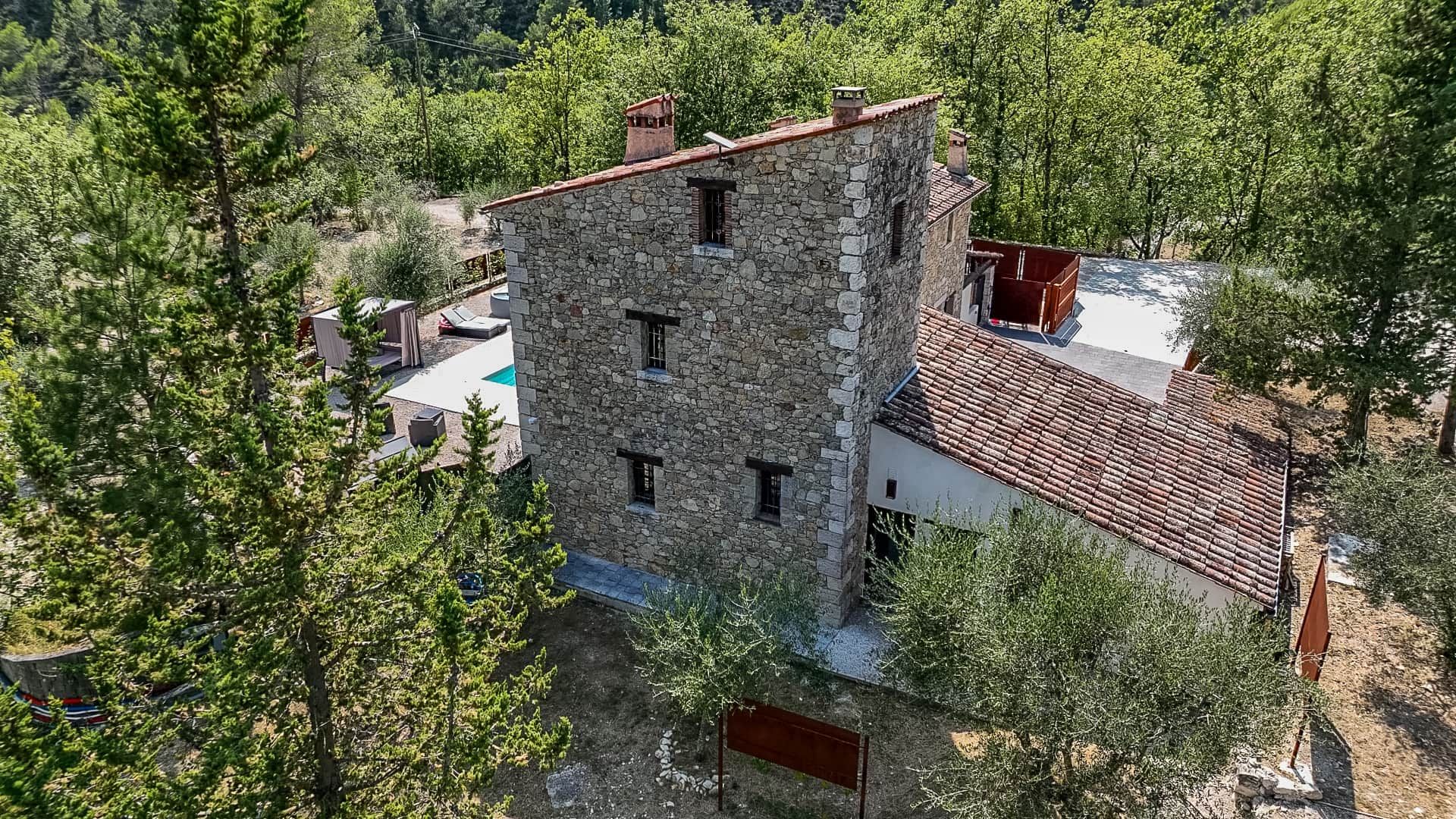 A stone building with a red-tiled roof, surrounded by trees.