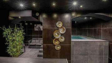Un espace spa moderne comprenant un jacuzzi, un panneau décoratif fixé au mur et un coin salon avec un canapé et une plante.