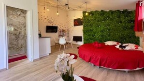 A modern bedroom with a red bed, a green wall, and a small desk area. - Love Room—Air-Conditioned Jacuzzi Area / Massage Table (L'Escarène)