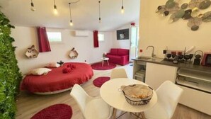 A compact living space with a bed, a dining area, and a kitchenette. - Love Room—Air-Conditioned Jacuzzi Area / Massage Table (L'Escarène)