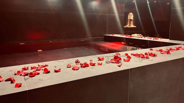 A room with a long table covered in red rose petals, a statue, and a large mirror reflecting the room. - Love Room—Air-Conditioned Jacuzzi Area / Massage Table (L'Escarène)