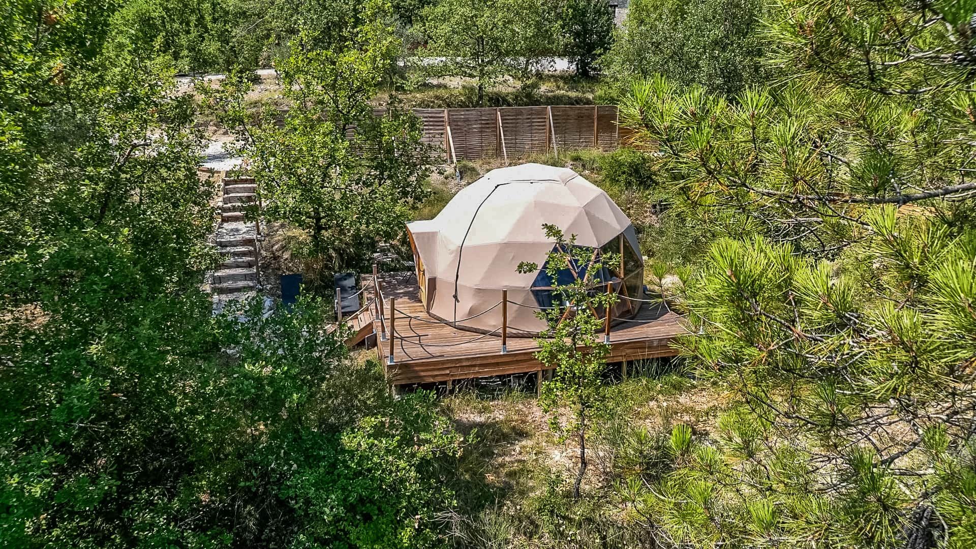 A geodesic dome structure with a wooden deck, surrounded by dense greenery.