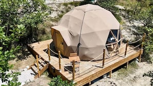Une tente en forme de dôme dotée d’une terrasse en bois et d’une petite table, le tout entouré d’une végétation naturelle.