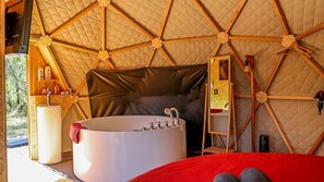 A tented accommodation with a large bathtub, a mirror, and a red bed. - Dome & Balneotherapy (L'Escarène)