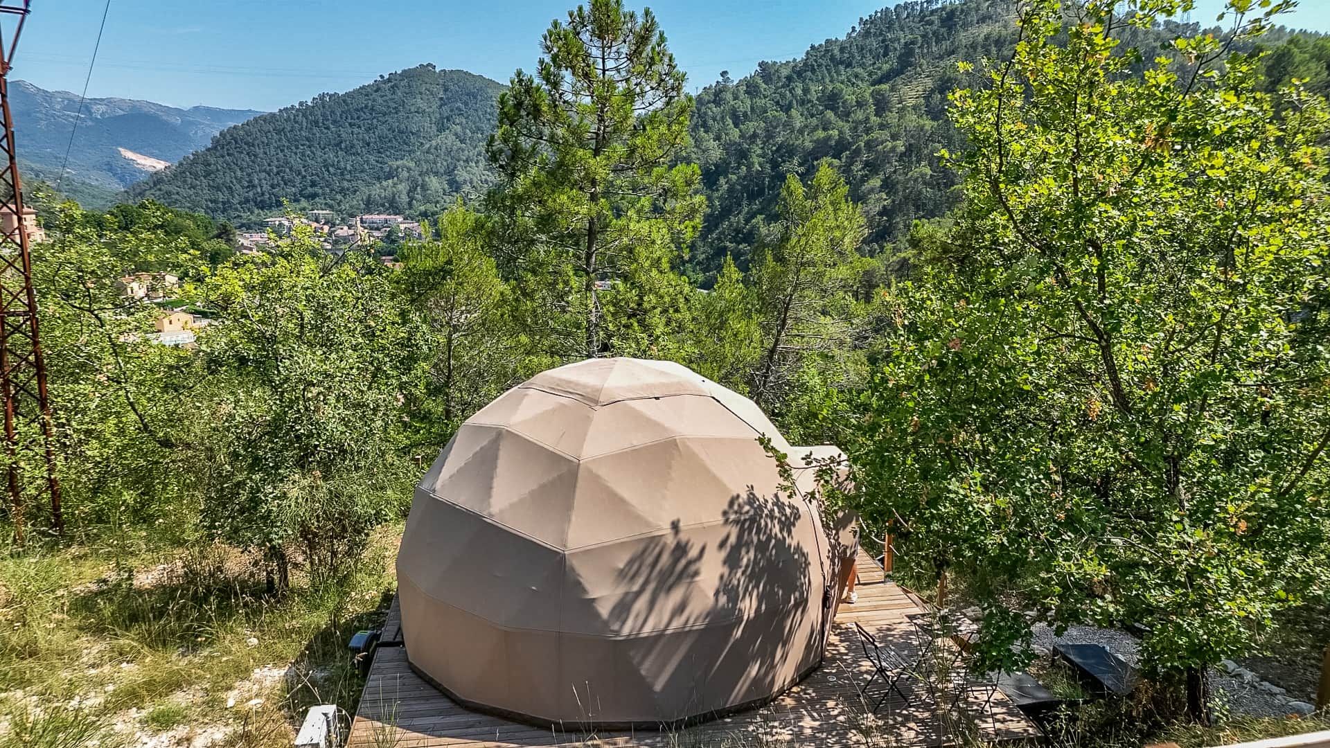 A geodesic dome structure in a natural setting with trees and a mountainous backdrop.