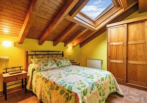 A bedroom with a skylight, wooden ceiling beams, a bed with floral bedding, a nightstand, and a wardrobe. - Rural Apartments La Viña (Apartment number 9) (Cangas de Onis)