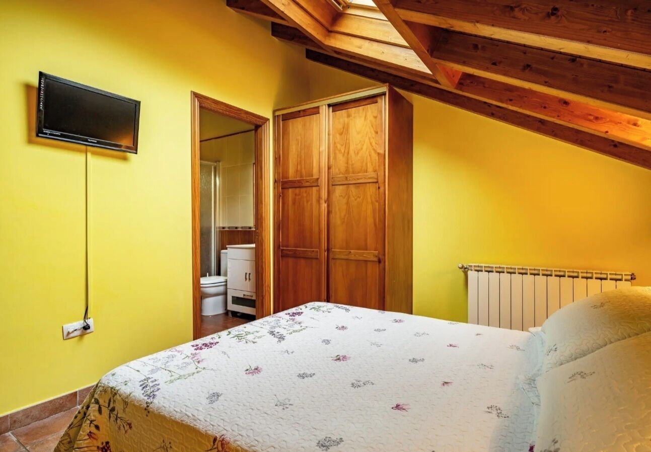 Ein Schlafzimmer mit einem Bett, einem an der Wand befestigten Fernseher, Holzschränken und einer Heizung.