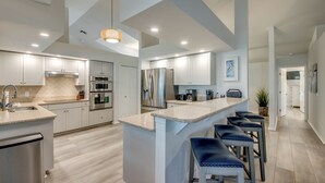 A modern kitchen with white cabinetry, stainless steel appliances, and a central island with bar stools. - Villa Tarpon Point Treasure – Stunning 4 BR direct access waterfront Escape with heated pool, bikes, and fishing poles - private guest wing (Cape Coral)