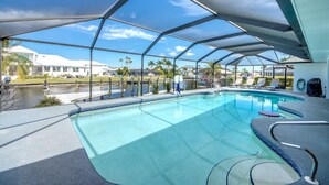 A swimming pool with a covered area, clear blue water, and a view of palm trees and buildings in the background. - Villa Tarpon Point Treasure – Stunning 4 BR direct access waterfront Escape with heated pool, bikes, and fishing poles - private guest wing (Cape Coral)