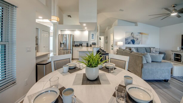 A modern kitchen with white cabinets, a dining area with a round table, and a living room with a sofa and a TV. - Villa Tarpon Point Treasure – Stunning 4 BR direct access waterfront Escape with heated pool, bikes, and fishing poles - private guest wing (Cape Coral)