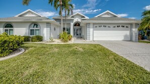A two-story house with a garage, a front entrance with a door, and a well-maintained lawn. - Villa Tarpon Point Treasure – Stunning 4 BR direct access waterfront Escape with heated pool, bikes, and fishing poles - private guest wing (Cape Coral)