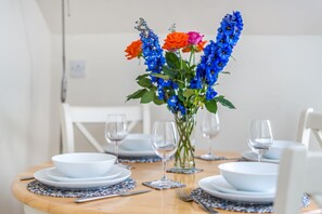 Une table à manger dressée avec de l’assiette, des bols et des couverts blancs, agrémentée d’un vase de fleurs.