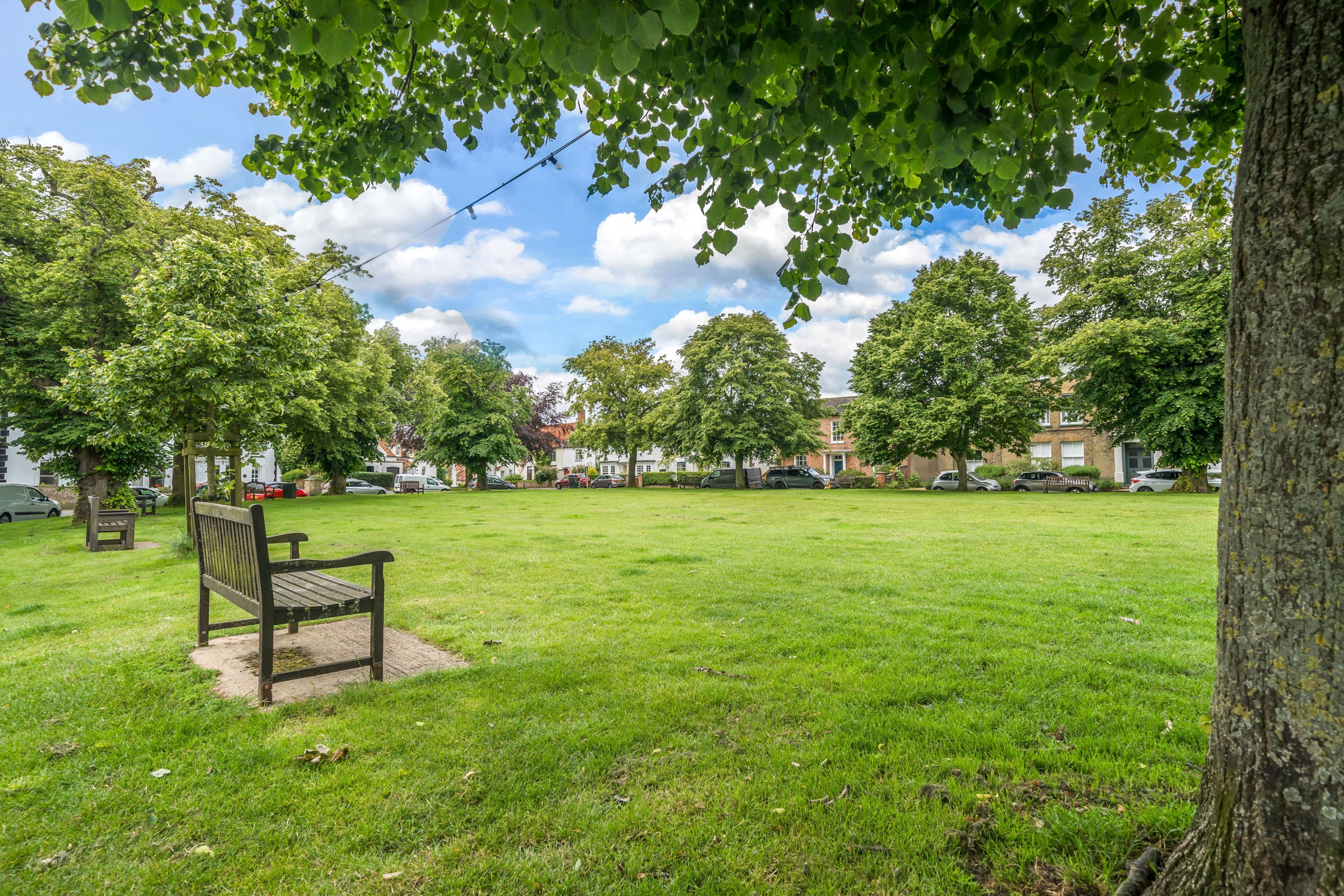 A park with a bench, trees, and a clear sky.