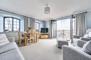A spacious living room with a dining area, a television, and a balcony with a view. - 6 The Granary - sleeps 2 guests  in 1 bedroom (Wells-next-the-Sea)