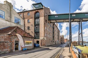 A street with a brick building, a blue car parked in front, and a green overhead structure. - 6 The Granary - sleeps 2 guests  in 1 bedroom (Wells-next-the-Sea)
