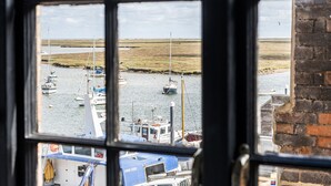 Udsigt gennem et vindue af en havn med fortøjede både, en græskrænt og en murstensbygning.