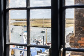 A view through a window of a marina with boats docked, a grassy shore, and a brick building. - 6 The Granary - sleeps 2 guests  in 1 bedroom (Wells-next-the-Sea)