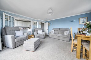 A spacious living room with a sofa, ottoman, and a dining area with a table and chairs. - 6 The Granary - sleeps 2 guests  in 1 bedroom (Wells-next-the-Sea)