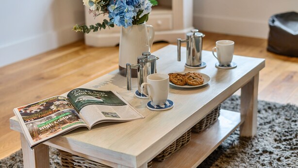 Ett träbord med ett tidningsnummer, en kaffekanna, en kopp och en tallrik med kakor.