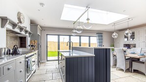 A modern kitchen with a central island, built-in appliances, and a dining area with wicker chairs. - Olive's Cottage - sleeps 6 guests  in 3 bedrooms (Burnham Market)