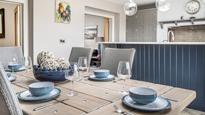 A dining area with a wooden table set for four, surrounded by wicker chairs. - Olive's Cottage - sleeps 6 guests  in 3 bedrooms (Burnham Market)